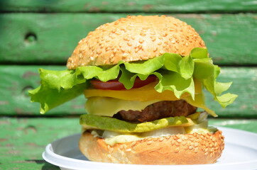 Beautiful grilled burger with onion, lettuce, tomatoes, beef, zucchini, sesame bun. Burger for grill party at sunny summer day. Close-up photo.