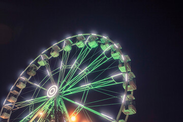 White fun wheel illuminated with green light against dark night sky. Christmas market theme. Soft and dreamy look. Selective focus.