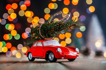 Christmas trees delivery background, red toy car with fir tree against colorful Christmas lights bokeh