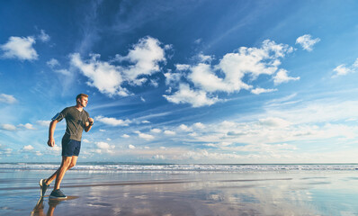 Fototapeta na wymiar Sports lifestyle. Happy young man in earphones jogging on the sea shore.