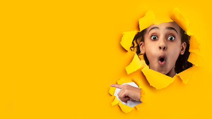 Shocked african american teenage girl with open mouth looks through hole on yellow paper