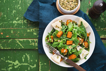 Warm salad with arugula, baked pumpkin, cheese and pumpkin seeds on a rustic background