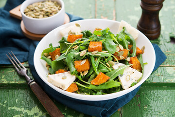 Warm salad with arugula, baked pumpkin, cheese and pumpkin seeds on a rustic background