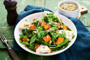 Warm salad with arugula, baked pumpkin, cheese and pumpkin seeds on a rustic background, selective focus