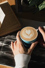 Cappuccino coffee in a blue ceramic mug in the sunbeams in a light cafe with a book in his hands