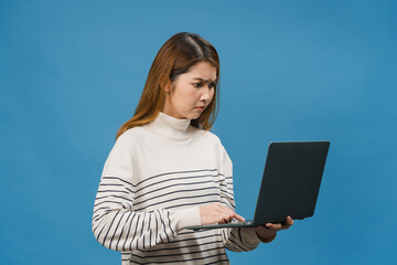 Young Asia lady using laptop with negative expression, excited screaming, cry emotional angry in casual cloth and stand isolated on blue background with blank copy space. Facial expression concept.