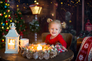 Obraz na płótnie Canvas Cute little blond child, curly girl with two ponytails, sitting on a table with christmas decoration, writing letter and playing with toys