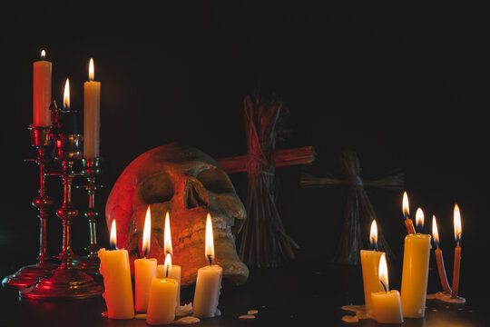 Old Skull and candle with incense on old altar plate which has dim light. Select focus, black background. Straw voodoo dolls. Copy space