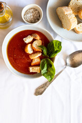 Top view of Spanish tomato soup, gazpacho  served in the bowl with bread crumbs, olive oil and salt on white tablecloth .