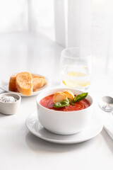 Tomato soup plate decorated with bread crumbs, fresh basil  and herbs on the restaurant table  at the window and served with glass  of water ,bread  and salt a