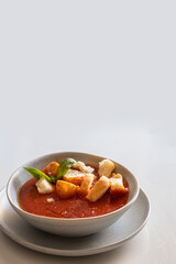 Italian tomato cream soup in grey bawl  with basil and herbs, served with toasted bread crumbs on white table.