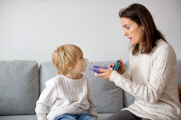 Mother, helping little toddler child with inhaler with spacer - obrazy, fototapety, plakaty