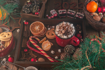 In a wooden tray there is a mug with marshmallows and New Year's attributes