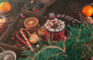 In a wooden tray there is a mug with marshmallows and New Year's attributes