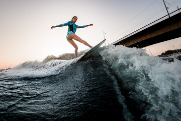 active woman energetically balancing on great splashing wave on wakesurf.