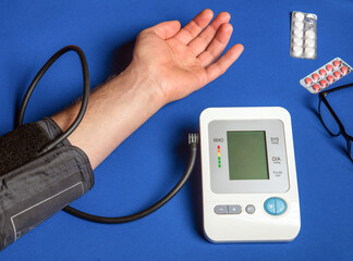 Person measures their own blood pressure at the blue medical table. Taking care of your own health.