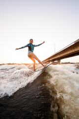 handsome woman energetically balancing on great splashing wave on wakesurf.