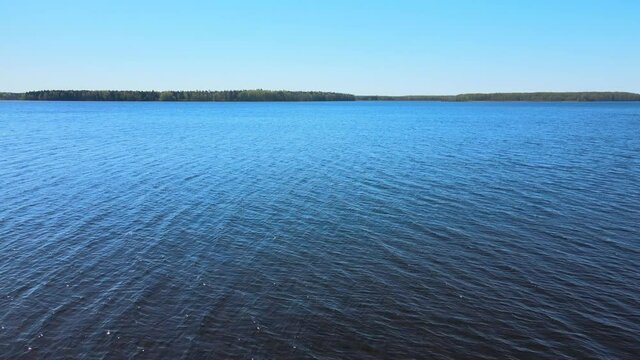 Russia, Moscow region,Pushkino, Uchinskoe reservoir(Akulovskoe reservoir). Aerial video of a flight over the blue expanse of water in sunny weather. Forest in the distance, small waves.