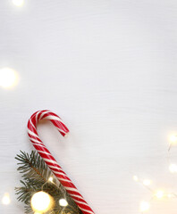 striped lollipop staff and fir branch on a light background with lights of garlands. sweet festive...