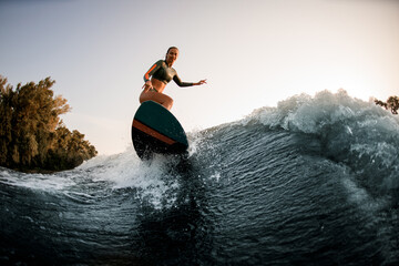 Athletic wet woman making trick with wakesurf on splashing wave.