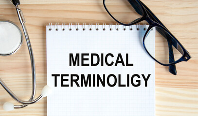 In the notebook the text MEDICAL TERMINOLIGY, next to it are a stethoscope and glasses.