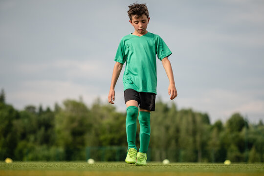 Junge mit Blick am Fußballrasen geht alleine am Fußballplatz mit Wald im Hintergrund