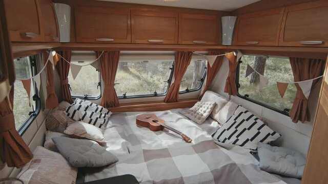 Tracking with slowmo of interior of cozy camper. Ukulele lying on bed and fabric flags garland hanging on windows