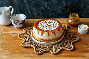 cheesecake with caramel and almonds on a white plate and a wooden board. Side view, green and wooden background.