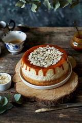 cheesecake with caramel and almonds on a white plate and a wooden board. Side view, green and wooden background.