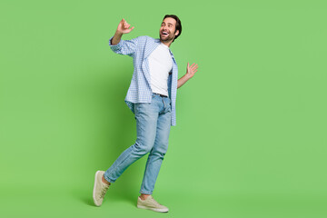 Full size photo of joyful millennial guy move look empty space wear shirt jeans shoes isolated on green color background