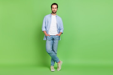 Fototapeta na wymiar Full length photo of cool young guy stand wear shirt jeans sneakers isolated on green color background