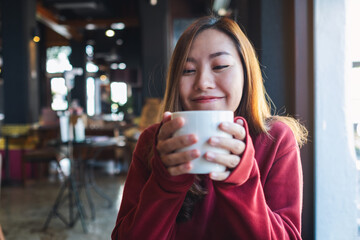 A young woman holding and drinking hot coffee in cafe