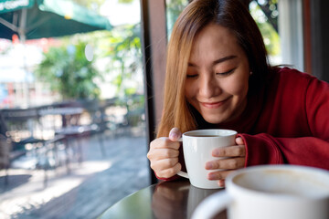 A young asian woman holding and drinking hot coffee in cafe