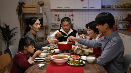 asian extended family blowing and tasting the hot delicious soup with spoons while they are...