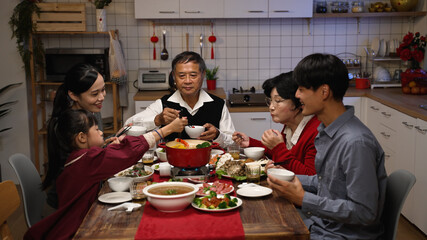 happy asian family members picking food from hot pot with chopsticks while enjoying traditional reunion dinner at home on chinese new year’s eve