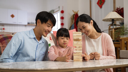 asian father and mother clapping hands for their girl daughter who is learning to play jenga in the living room at home with festive decoration during chinese spring festival