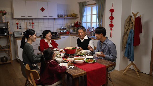 happy asian extended family laughing at the man’s joke while having reunion dinner on chinese new year’s eve in a cozy festive home interior