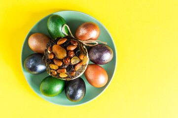top view of a green ceramic plate with An Easter cake and painted eggs on a yellow background.