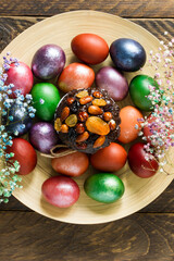 Easter cake with dried fruits and nuts on a large wooden plate with colored eggs. top view. vertical image.