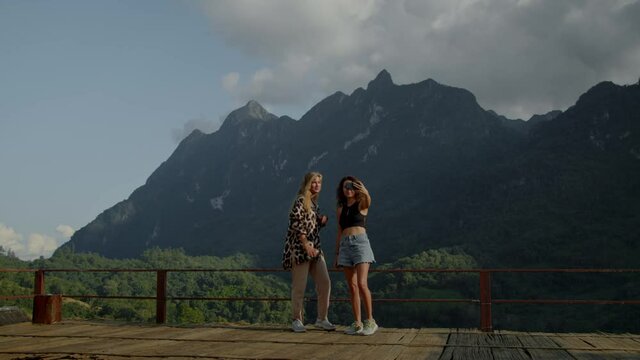 Two young women photographed against the mountain view, enjoying their vacation, travel adventure.