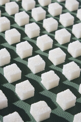 Refined sugar on green background.Cubes of sweet and white sugar in geometricshape. Hard shadows.