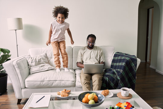 Multiracial father holding laptop at his knees and sitting at the sofa