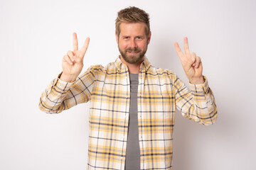 Naklejka premium Handsome young man with beard wearing plaid shirt smiling looking to the camera showing fingers doing victory sign.