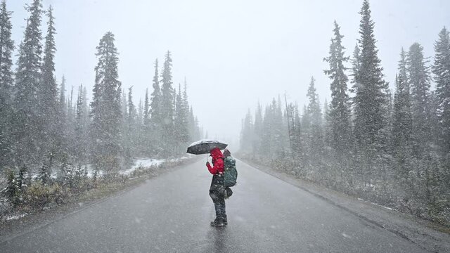 Man backpacker holding umbrella in blizzard on the road in the forest