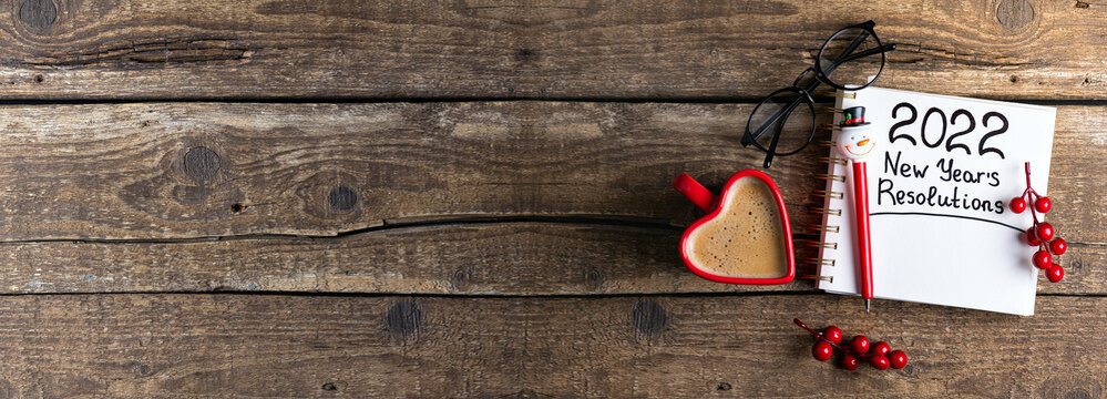 New year resolutions 2022 on desk. 2022 new year resolutions on wooden background with coffee cup, notebook and christmas decorations. New year goals, plan, resolutions, business concept. Copy space