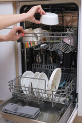 Female hands put dirty dishes in the dishwasher. Close-up of the dishes placed in the dishwasher....