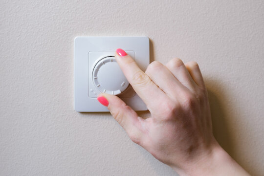Woman's hand adjusts the lighting with a dimmer lever. An electronic device designed to change electrical power. Used to adjust the brightness of the light emitted by incandescent lamps or LEDs.