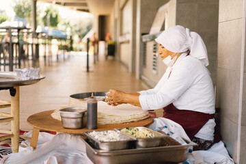 Turkish Woman making Tortillas on a wooden rustic table. A cook prepares tortillas with different fillings at a street in the summer.