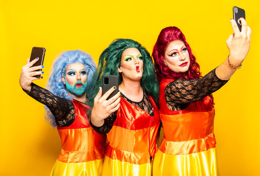 Drag queens taking selfie through mobile phones against yellow background