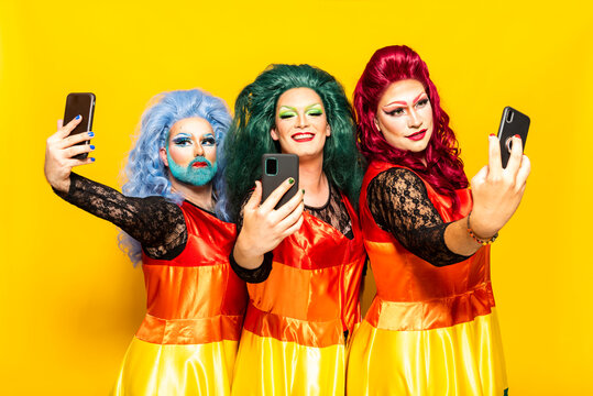 Drag queens taking selfies through smart phones against yellow background